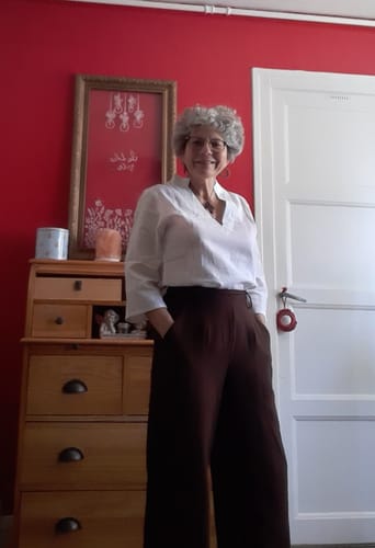 Cliente portant son Pantalon Tino chocolat à la coupe large, posant avec les mains dans les poches.