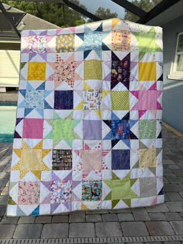 Reviewer's finished Cut Flowers quilt, made from many colorful scrap fabrics, held up outdoors.