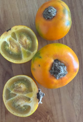 Kundenfoto von ganzen und halbierten Lulo-Früchten, die ihr grünes Fruchtfleisch auf einem Holztisch zeigen.