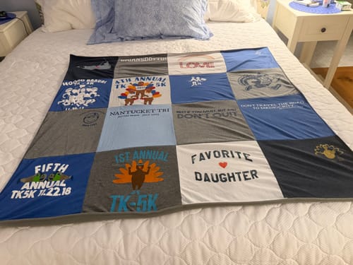 Customer's completed Project Repat T-Shirt Quilt, a grid of colorful t-shirt panels, spread neatly on a bed.