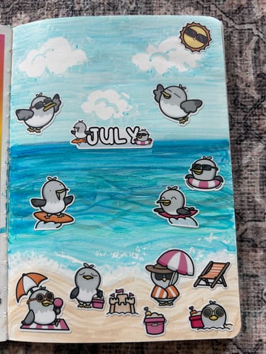 Customer's journal page showing a creative beach scene made with penguin stickers from the Ultimate Subscription.