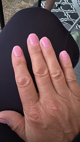 Hand einer Kundin mit manikürten Nägeln, die das glänzende UV-Gel in Lovely Pink trägt.