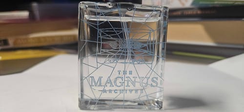 Reviewer's Ex Altiora perfume bottle, showing the intricate, web-like engraving from The Magnus Archives.