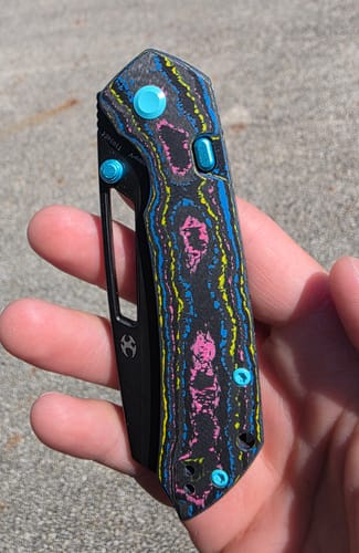 Customer holding the folded KANSEPT Fenrir knife with a vibrant Jazzy Camo Carbon handle and turquoise hardware.