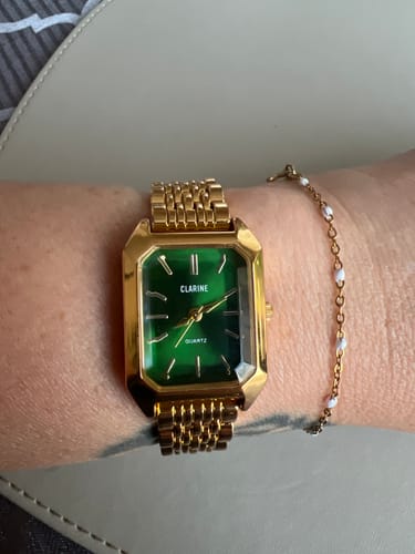 Customer's wrist wearing the gold CLAIRE DE MAINS watch with a rectangular green face.