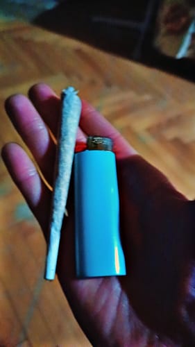 Customer's hand holding a rolled joint of Lemonatti flower and a light blue lighter.