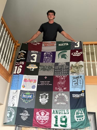 Customer holding a large Project Repat T-Shirt Quilt made from various shirts, draped over a staircase railing.