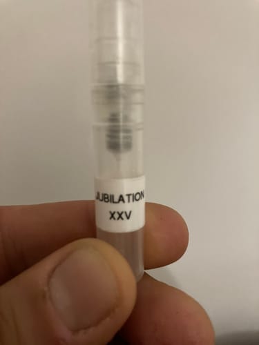 Primo piano della mano di un cliente che tiene un campioncino dell'eau de parfum Jubilation XXV Man.