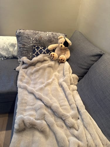Kundes beige Galena pledd som ligger mykt og dekorativt på en grå sofa.