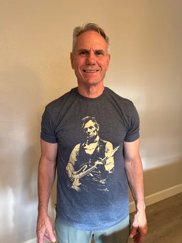 Reviewer smiling while wearing the dark grey Lincoln Guitar T-Shirt.
