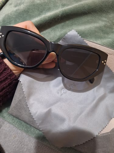Cliente sosteniendo los Lentes de Sol con punta cuadrada negros sobre su paño de limpieza.