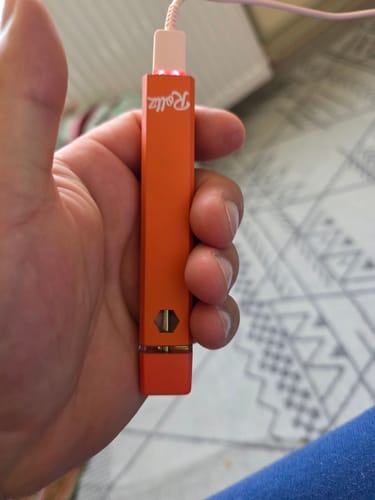 Customer holding the orange THC-A Vape in hand while it's plugged in and charging, showing a red light.