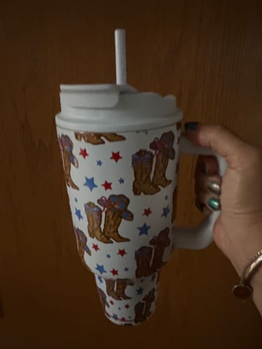 Customer holding the white 'All American Sweetheart' 50oz tumbler with a handle, showing its cowboy boot and star pattern.