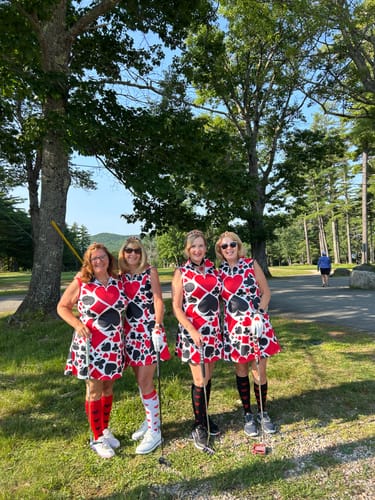 Four reviewers wearing matching Poker sleeveless golf dresses as a team on a golf course for a themed tournament.