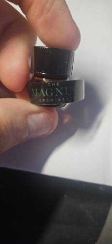 A customer's hand holding a small sample vial of the Jon and Martin perfume labeled 'The Magnus Archives'.