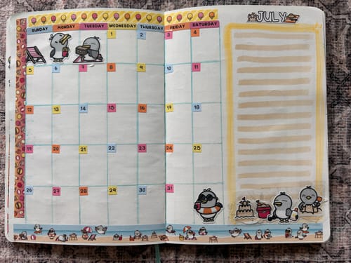 Reviewer's monthly planner spread for July decorated with penguin stickers and washi tape from the Ultimate Subscription.