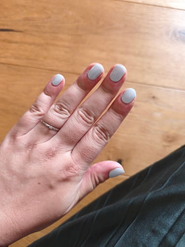 Hand einer Kundin, die ihre kurzen Nägel mit den UV-Gel-Nagelfolien in hellem Meerschaumblau zeigt.