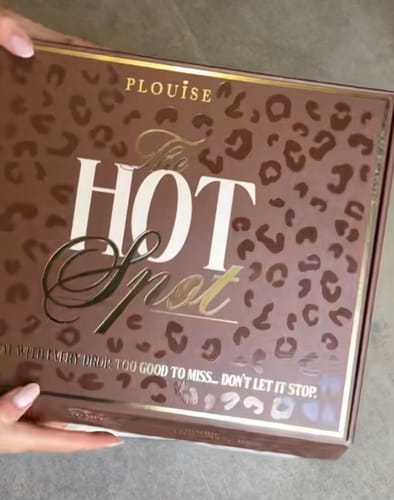 Reviewer holding the closed July Budget Box, showing its brown leopard print design and 'The Hot Spot' logo.