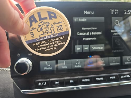 Customer holding a tin of Chilled Mint Nicotine Pouches in front of a car's dashboard.