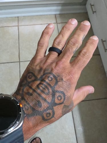 A customer showing their black silicone ring on a tattooed hand.