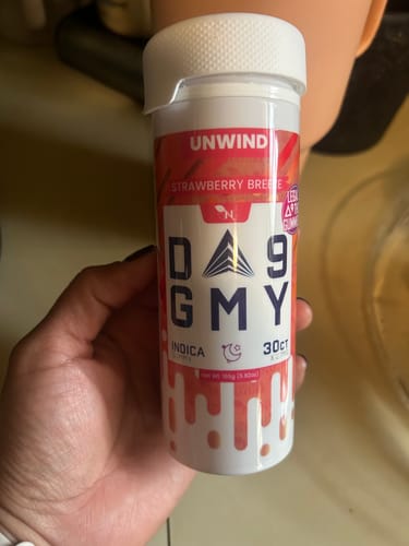 A reviewer's hand holding a white bottle of Unwind Delta 9 Strawberry Breeze gummies.