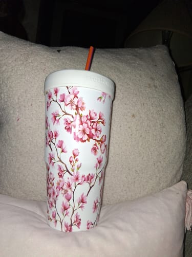 Customer's To-Go Buddy cup insulator with a pink cherry blossom pattern, resting on a pillow.