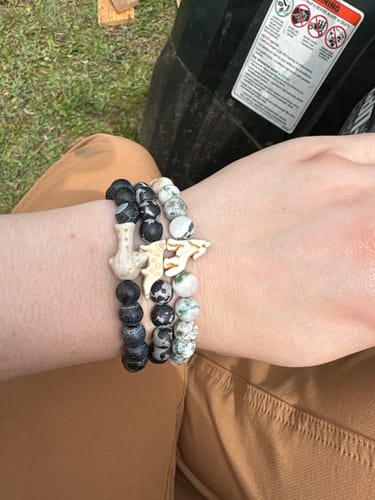 Customer's wrist showing The Scout Bracelet with a wolf charm, stacked with two other beaded animal bracelets.