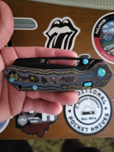 Customer holding the folded KANSEPT Fenrir knife, showing its colorful Camo Carbon handle and cyan hardware.