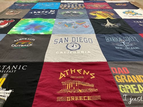 Customer's large, colorful Project Repat T-Shirt Quilt made from various travel and memory shirts laid flat.