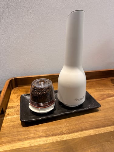 評論者的白色FinaMill電動香料研磨器，旁邊放著裝滿胡椒粒的研磨頭，放在托盤上。