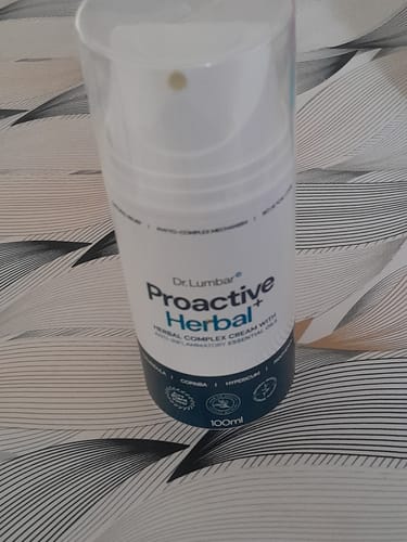 Customer's white and blue pump bottle of Proactive Herbal+ cream standing on a patterned surface.