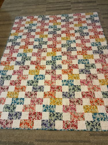 Reviewer's finished quilt from the Brick Prairie Precut Quilt Kit, showing the colorful floral and white square pattern.