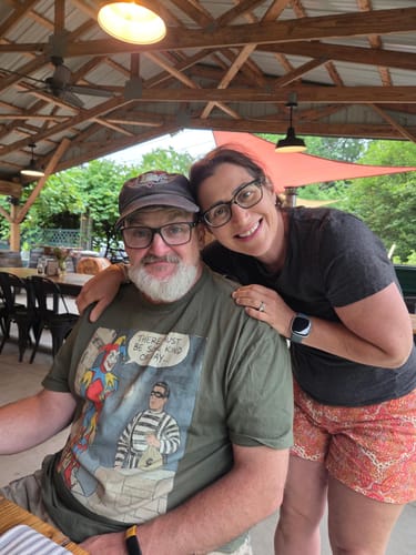 Reviewer wearing the graphic Watchtower T-Shirt while sitting at an outdoor table with a companion.