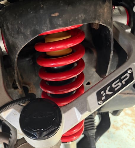 Close-up of a customer's silver KSP Aluminum Upper Control Arm installed over a red suspension coil.