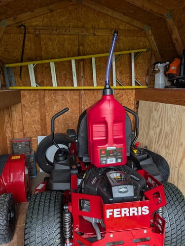 Customer's red 5 Gallon Jug sitting on the seat of a red riding lawnmower in a shed.
