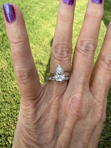Customer's hand showing the DovEggs pear-shaped diamond ring stacked with another band outdoors.