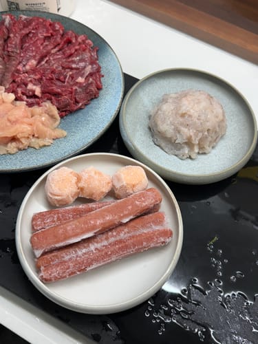 顧客用兩個 Vermicular 弧邊淺碟盛裝冷凍香腸和肉丸等火鍋食材。