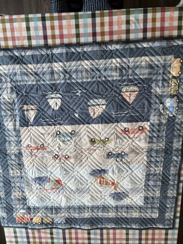 Customer's finished Busy Movers quilt, showing the vehicle print panel with diamond quilting and a plaid border.
