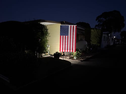 Customer's Ultra Heavy Duty American Flag illuminated by a bright spotlight on their house at night.