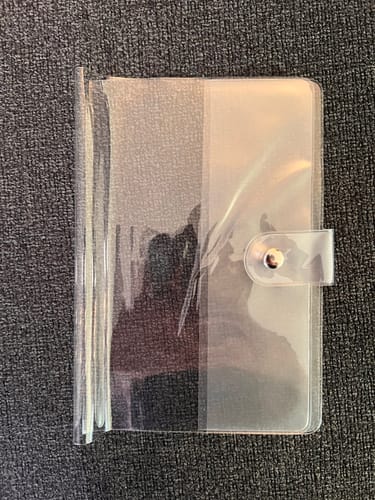 Customer's empty clear PVC journal cover lying flat with the snap closure fastened.