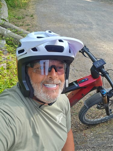 Reviewer smiling outdoors wearing Deathray™ Riding Glasses and a helmet, standing next to their mountain bike.