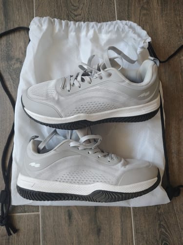 Customer's pair of light gray CUURT Muuv court shoes resting on top of a white drawstring bag on a wooden floor.