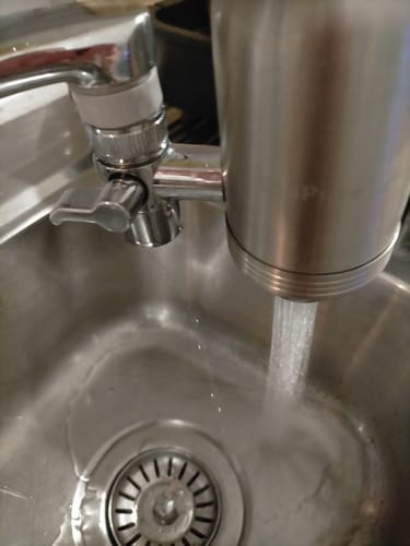 Customer's silver Tap Filter Unit installed on a kitchen faucet, dispensing water into the sink.