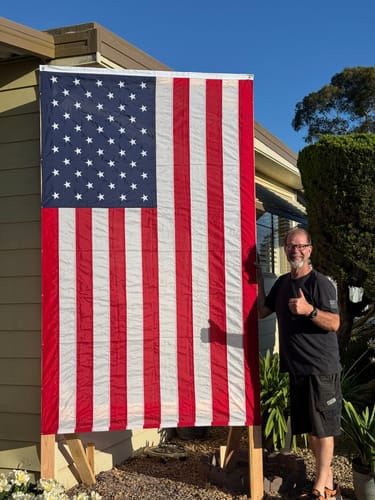 Reviewer gives a thumbs-up next to their large Ultra Heavy Duty American Flag displayed vertically outside their home.