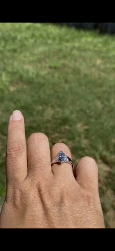 A customer's hand wearing a custom silver ring with a marquise-cut grey moissanite stone outdoors.