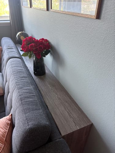 En kunde viser frem en lang, smal hylle bak en sofa, dekket med perlegrå kontaktplast.