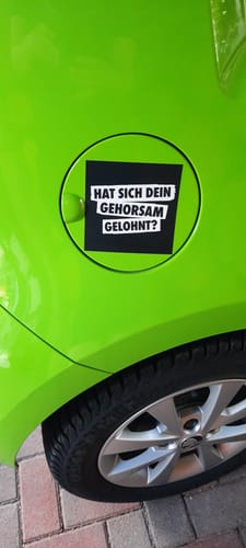 Kunde zeigt den quadratischen Aufkleber auf dem Tankdeckel eines leuchtend grünen Autos.