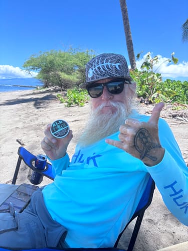 Customer sitting on a sunny beach in a chair, holding up a can of Refreshing Chill Nicotine Pouches.