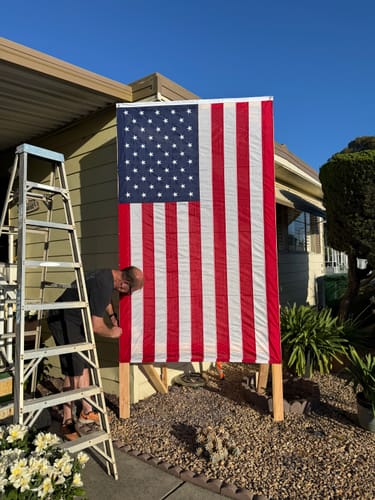 Customer setting up the large Ultra Heavy Duty American Flag on a wooden stand next to a ladder.