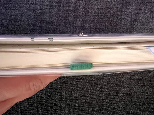 Close-up: A hand holds the journal, showing the side view of the clear journal cover and the pen loop slot.